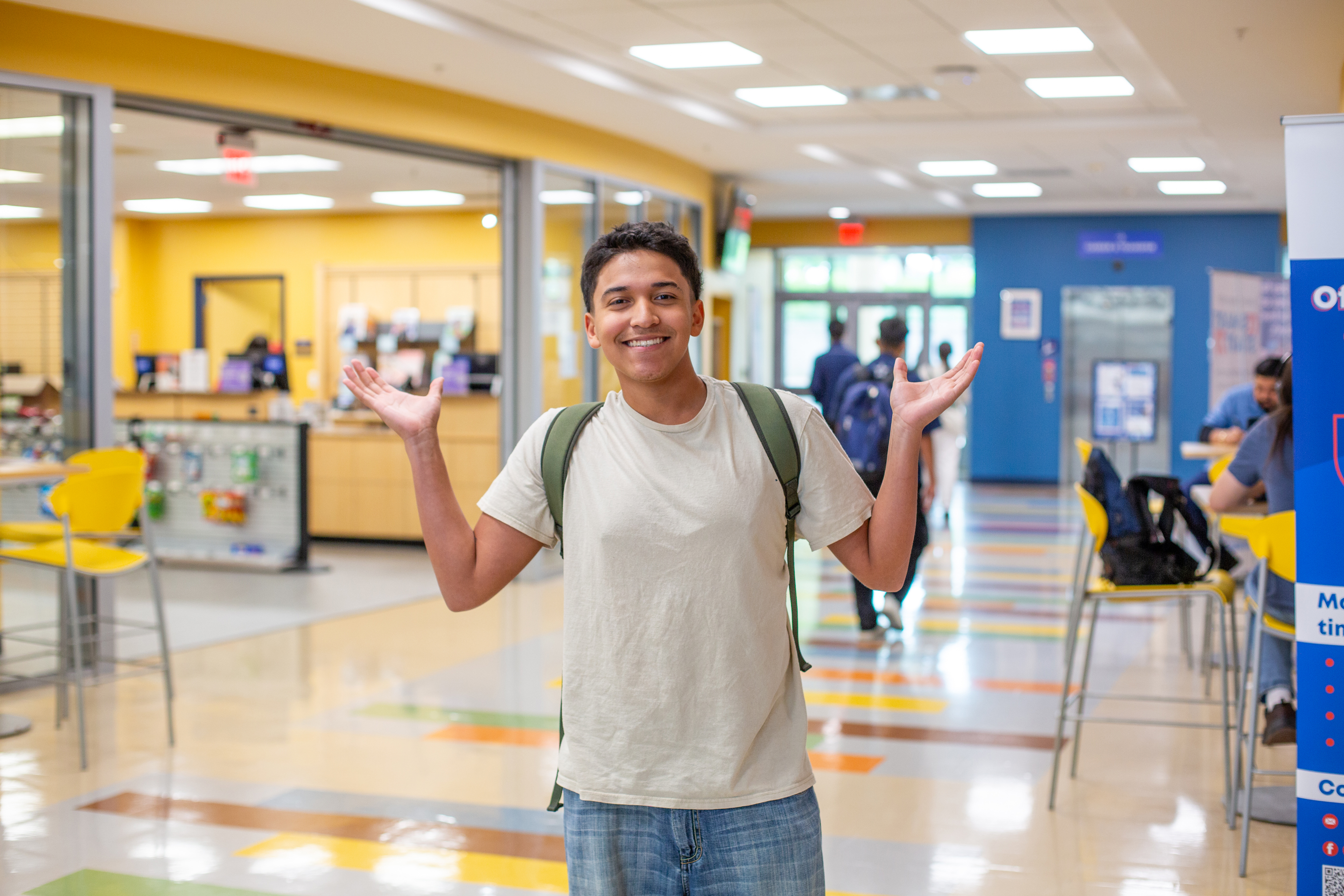 Student posing in hallway of a campus with arms lifted up.