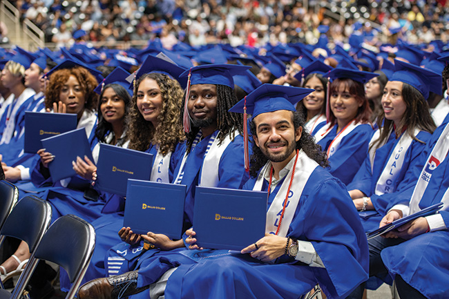 Dallas College graduates proudly holding up diplomas while seated and smiling at the camera