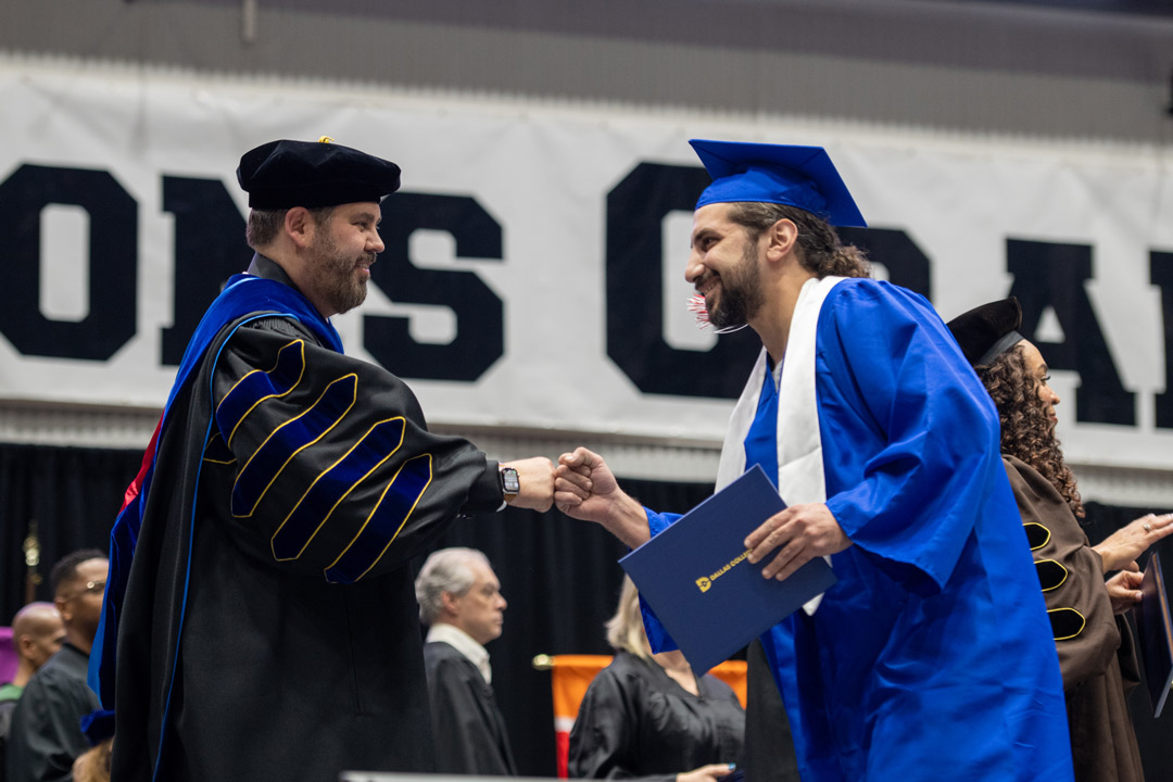 Dallas College graduate fist-bumps Dallas College's Chancellor, Dr. Lonon