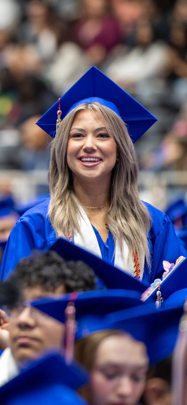 Smiling Dallas College graduate in cap and gown during commencement.