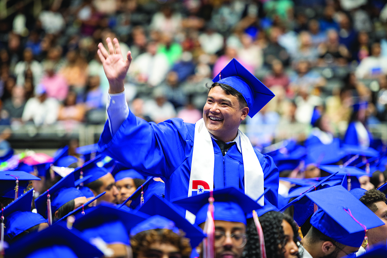 Dallas College graduate smiling at family and waving to crowd